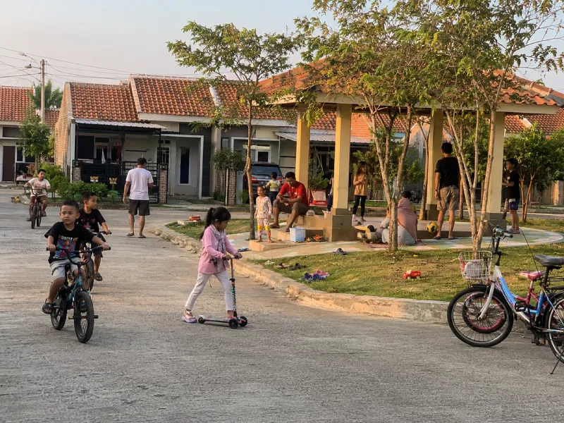 Anak kecil bermain sepeda di lingkungan perumahan cluster Bekasi sementara orang tua mengawasi